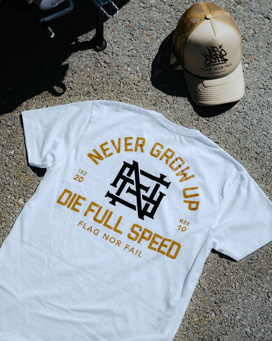 White t-shirt with text and logo on a concrete surface with a cap beside it.