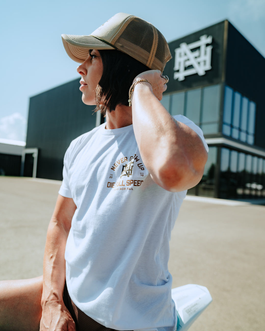 Person wearing a white t-shirt with text and graphics, sitting outdoors with a building in the background.