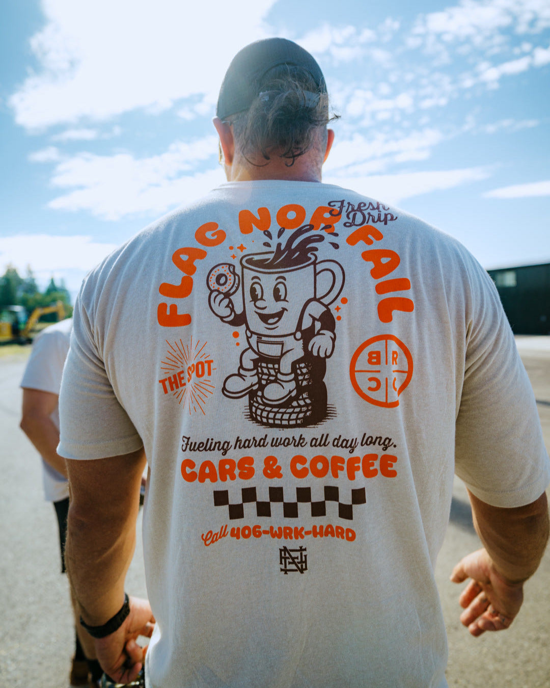 Man wearing a white t-shirt with a graphic design and text, standing outdoors on a sunny day.