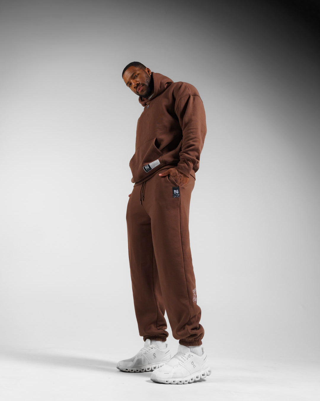 Person wearing a brown tracksuit with white sneakers on a gray background