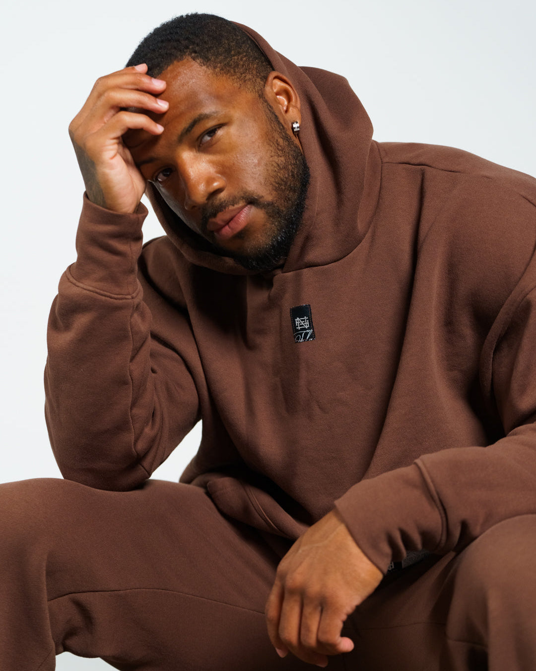 Man wearing a brown hoodie and pants sitting against a white background