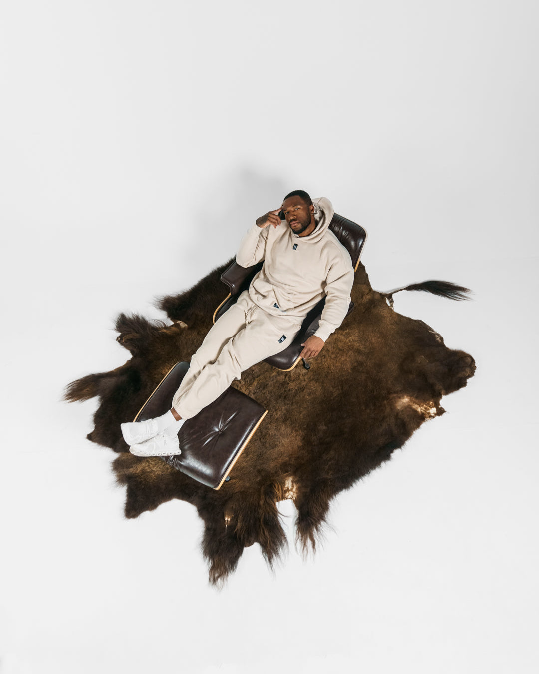 Man reclining in a chair on a large buffalo skin with a white background
