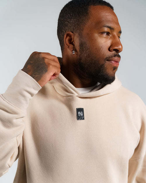 Man wearing a cream hoodie with a logo on a plain background