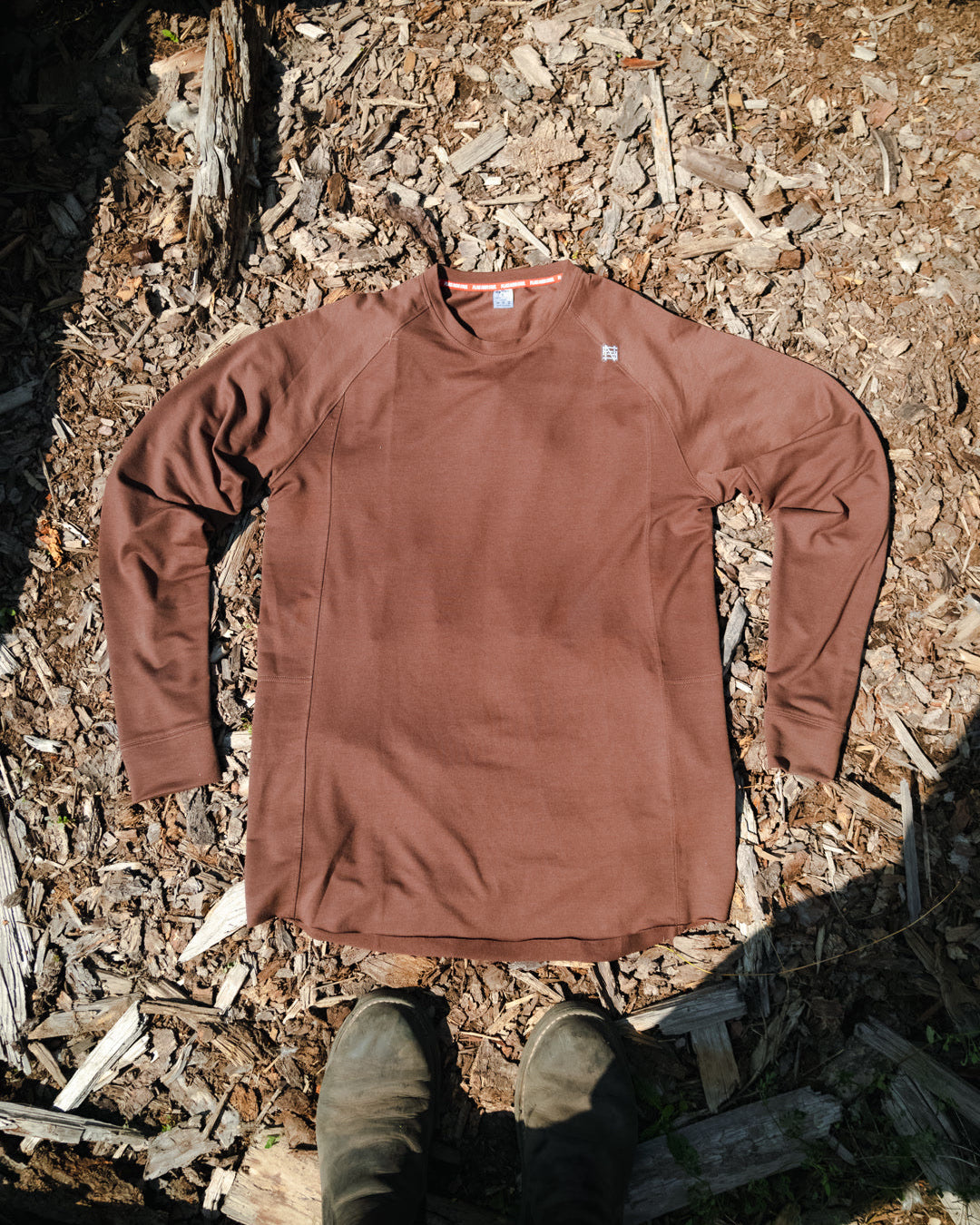 Brown long-sleeve shirt on a ground surface with shoes visible