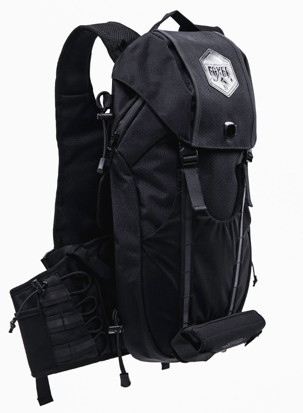The back of our Apex bag black in color. The top flap of the bag has a  hexagonal patch. The patch reads "ELEVATED OUTDOOR APPAREL" FGXFL above a range of mountains. The top flap has two buckles to buckle to the body of the pack. 